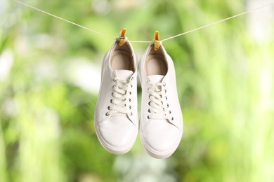 Photo of Stylish sneakers drying on washing line against blurred background