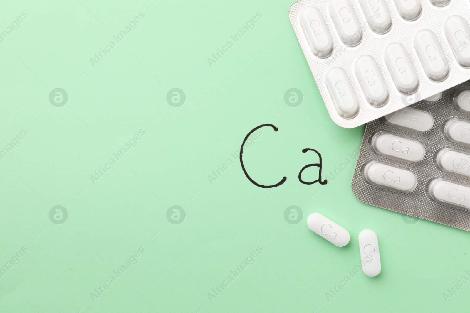 Photo of Blister packs with calcium supplement pills on light green background, flat lay. Space for text