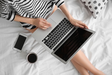 Photo of Female blogger with laptop and cup of coffee on bed, top view