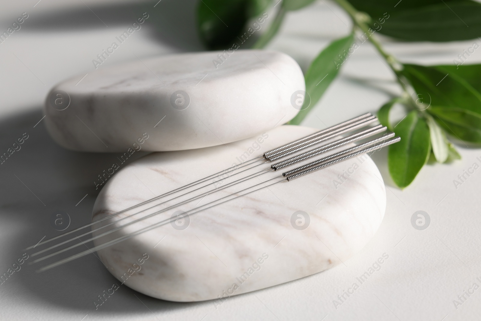 Photo of Stones with acupuncture needles on white table, closeup