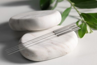 Stones with acupuncture needles on white table, closeup