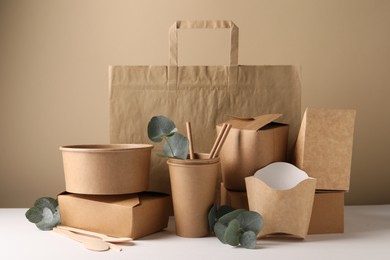 Eco friendly food packaging. Paper containers, tableware, bag and eucalyptus branches on white table against beige background