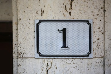 Plate with house number One hanging on beige old wall