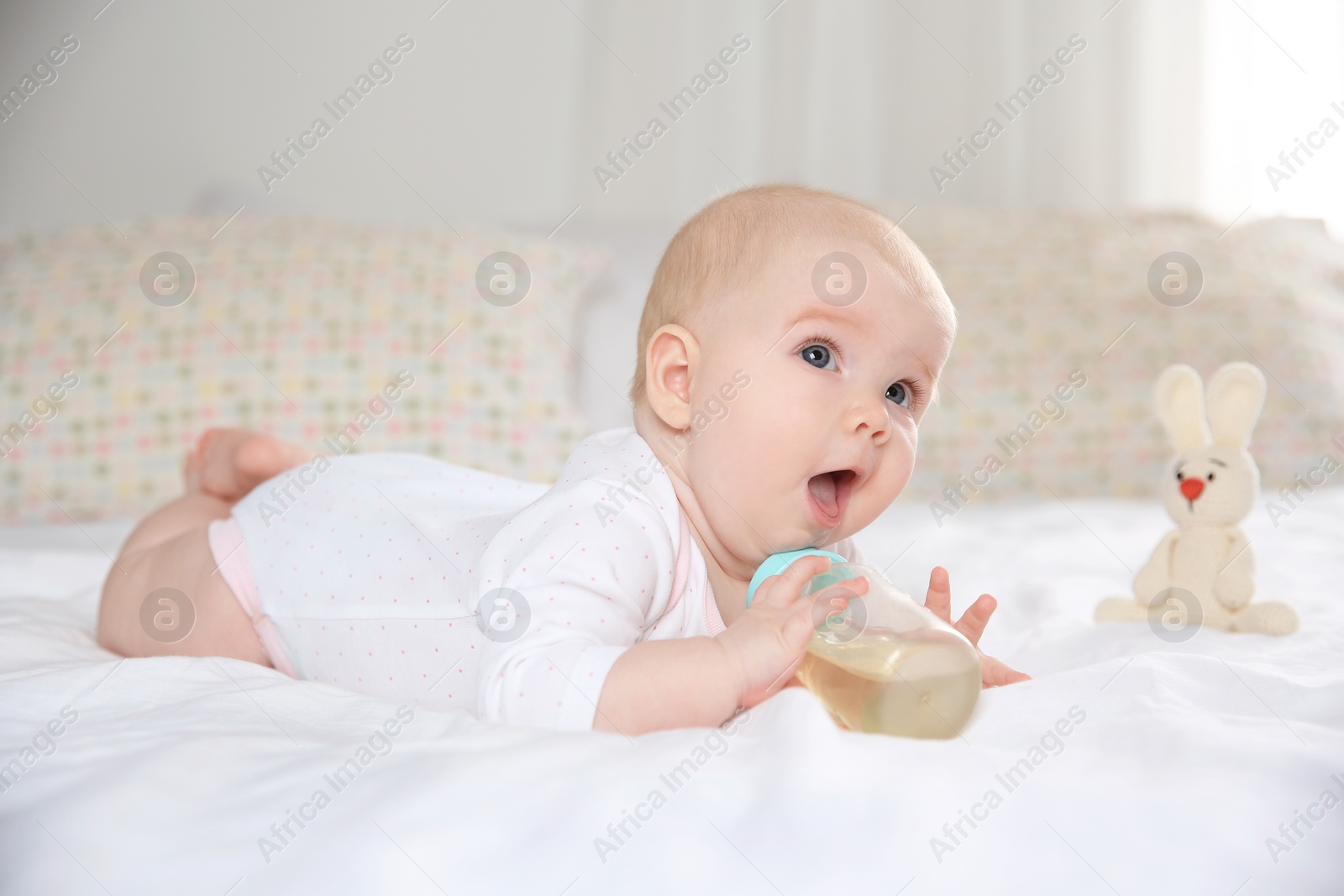 Photo of Pretty baby lying with bottle on bed at home