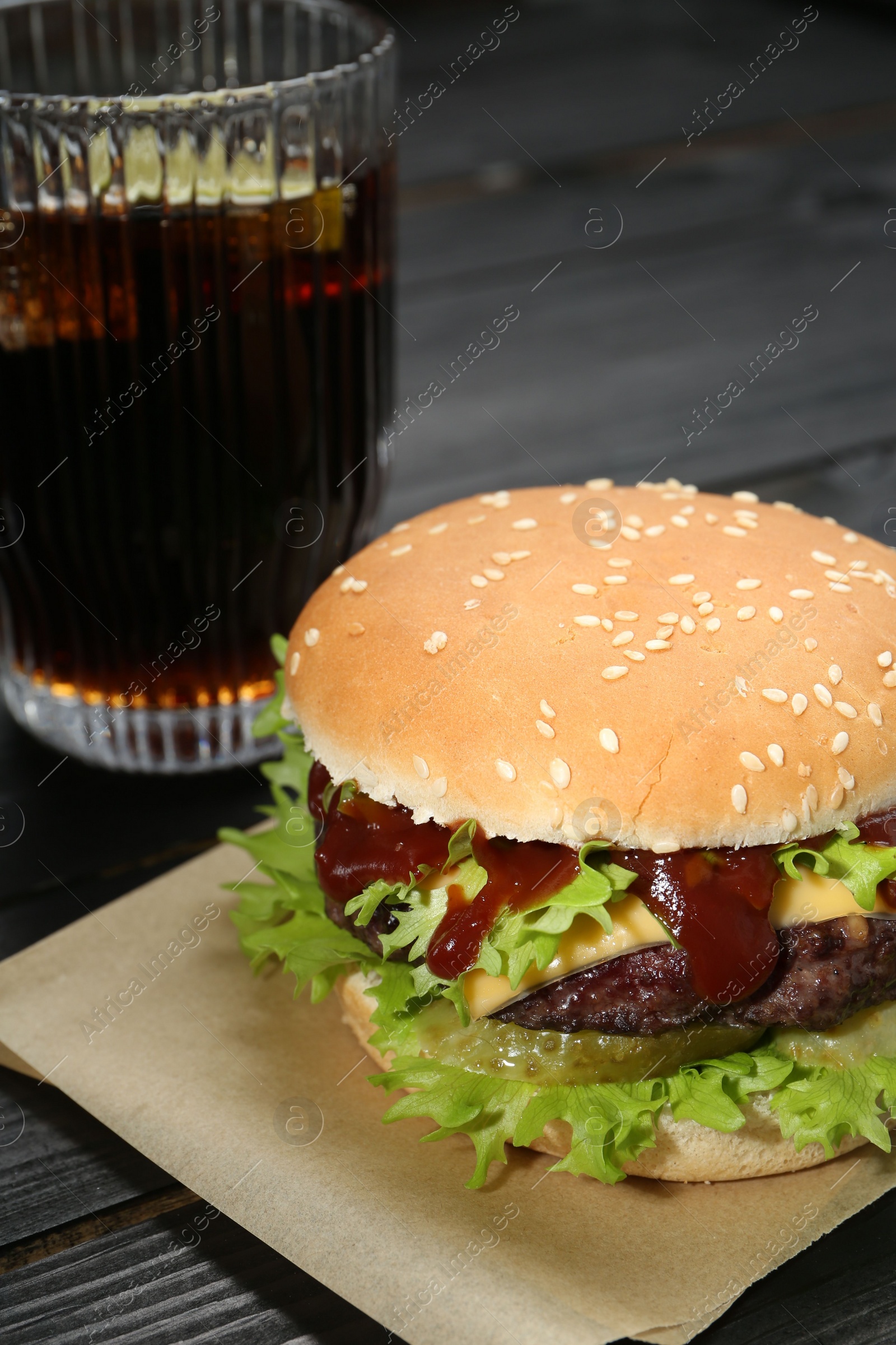 Photo of Burger with delicious patty and soda drink on black wooden table