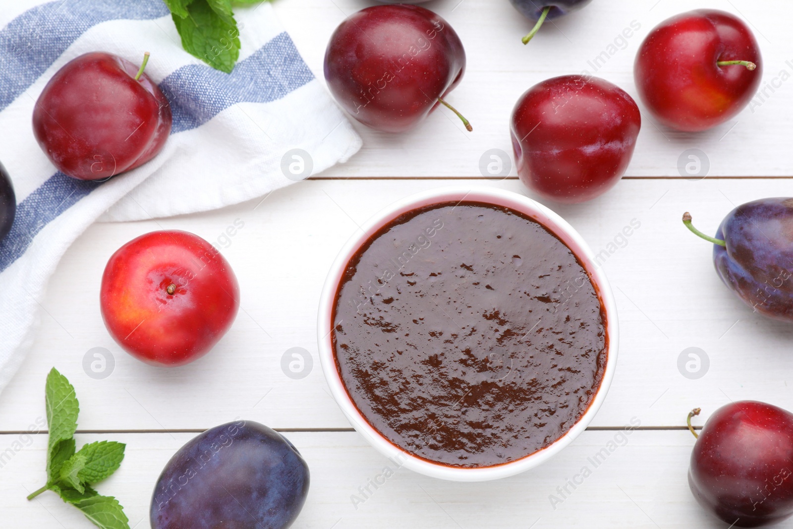 Photo of Plum puree in bowl and fresh fruits on white wooden table, flat lay