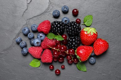 Many different fresh ripe berries and green leaves on dark grey table, flat lay