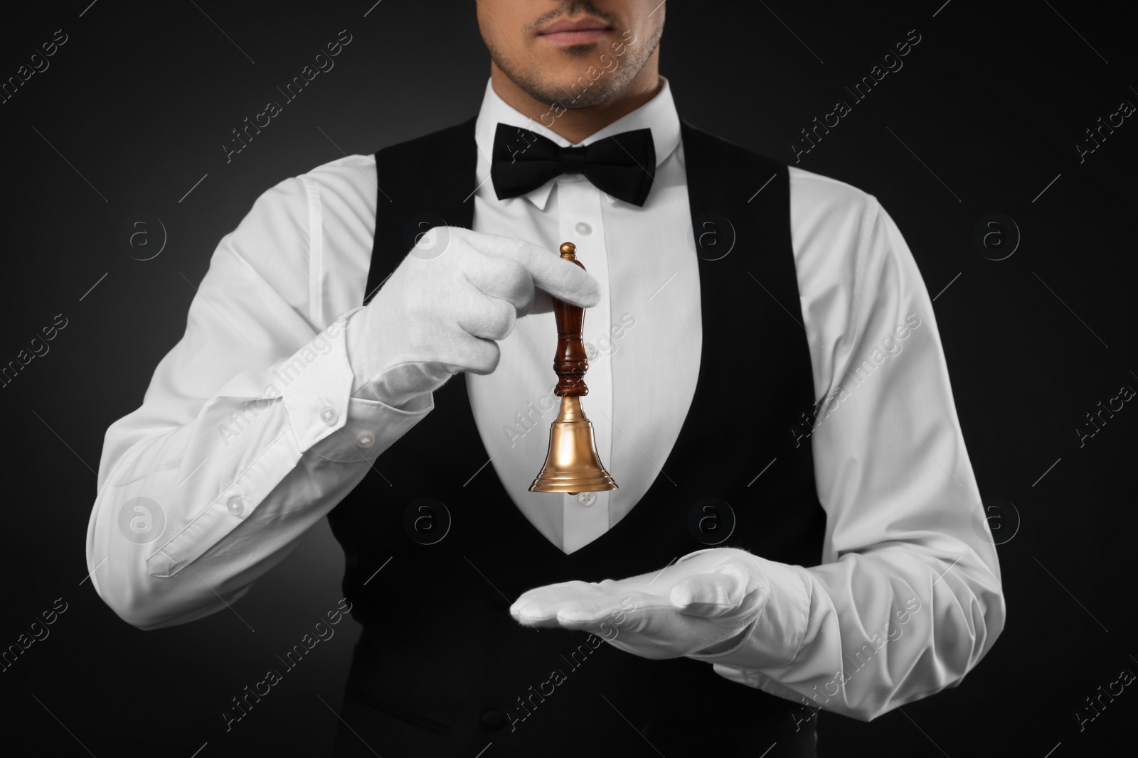 Photo of Butler holding hand bell on black background, closeup