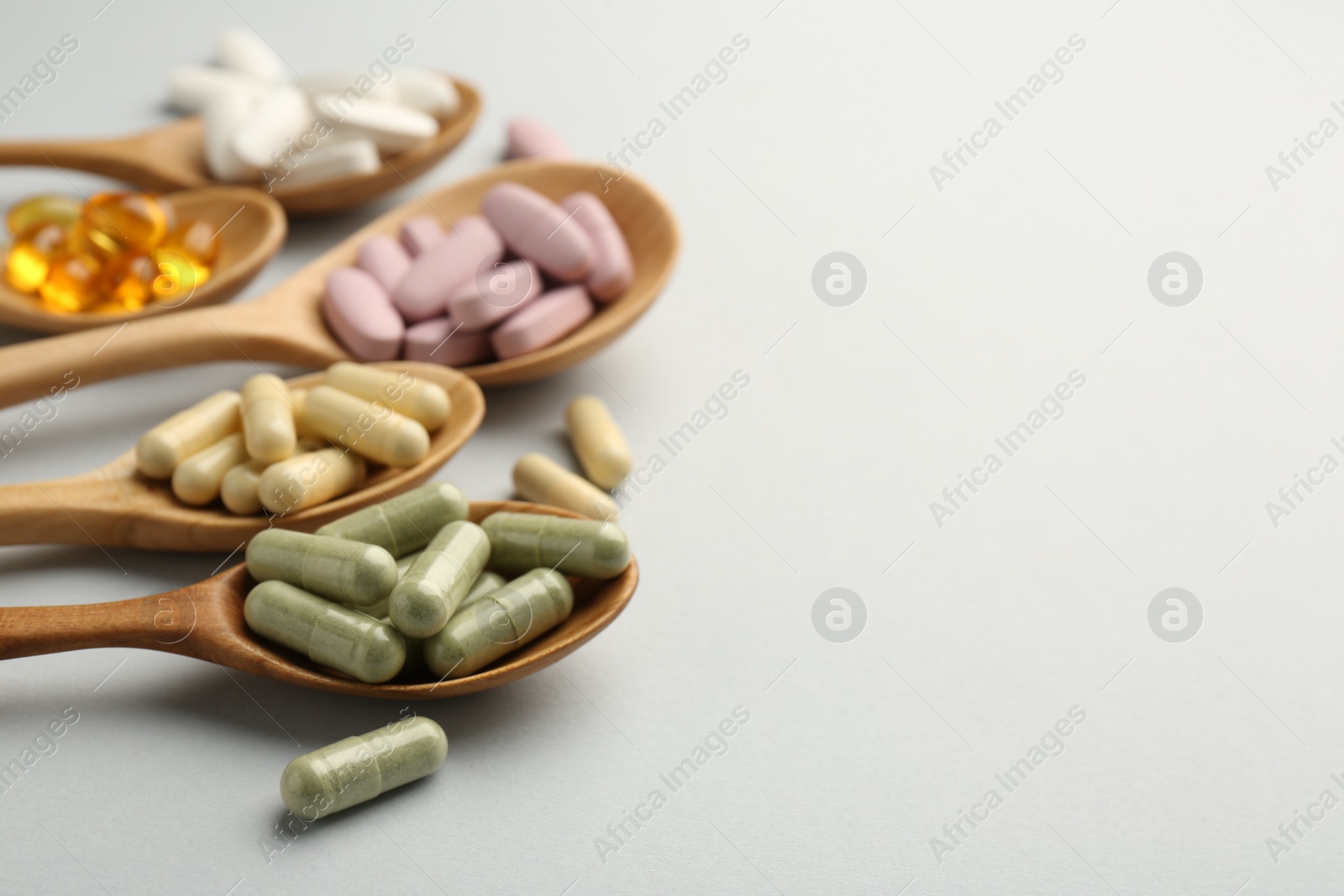 Photo of Different vitamin pills in spoons on light grey background, closeup with space for text. Health supplement