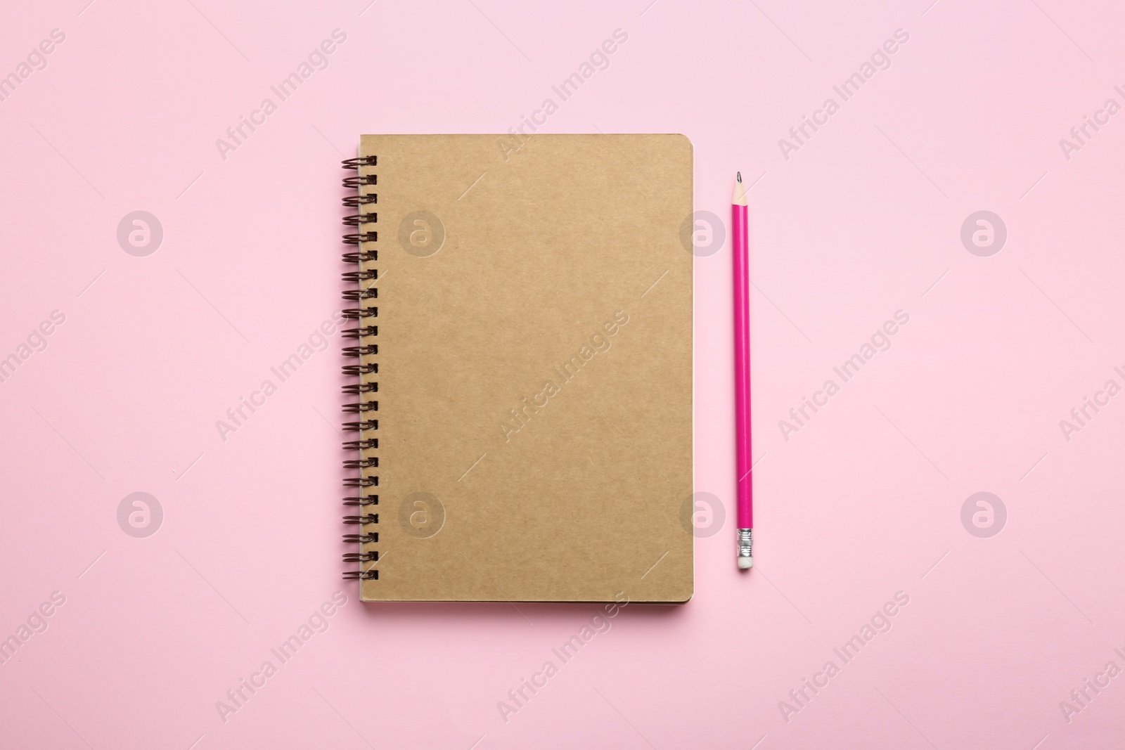 Photo of Notebook and pencil on pink background, top view