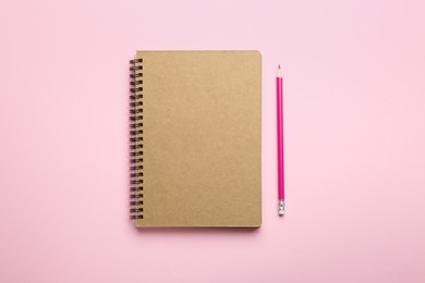 Notebook and pencil on pink background, top view