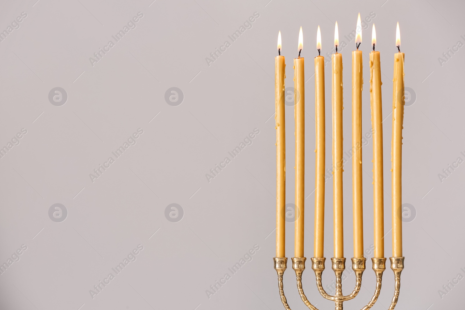 Photo of Golden menorah with burning candles on light grey background, space for text