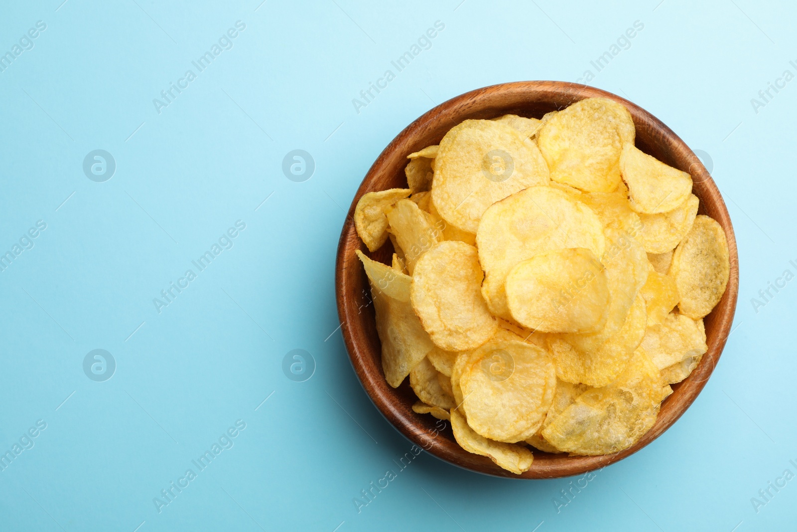 Photo of Delicious crispy potato chips in bowl on color background, top view with space for text