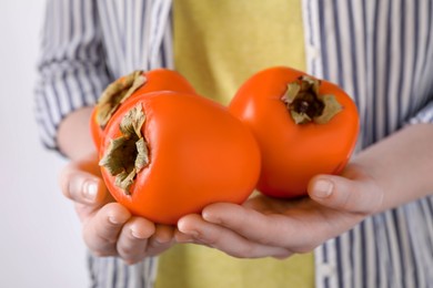 Photo of Woman holding delicious ripe juicy persimmons on light background, closeup