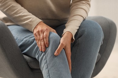 Mature woman suffering from knee pain in armchair, closeup. Rheumatism symptom