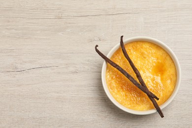 Photo of Delicious creme brulee and vanilla sticks on white wooden table, top view. Space for text