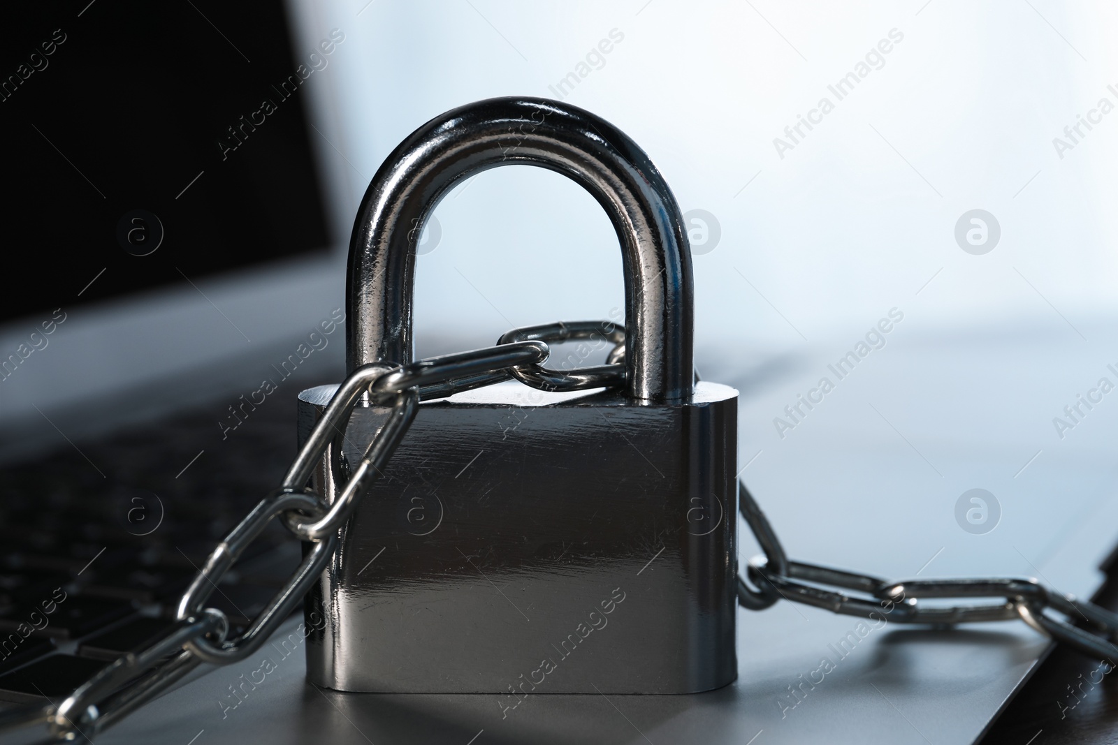 Photo of Cyber security. Laptop with padlock and chain on table, closeup