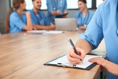 Photo of Medical student with clipboard and his groupmates studying in university library, closeup