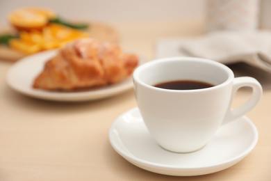 Photo of Cup of hot aromatic coffee and tasty croissant on table