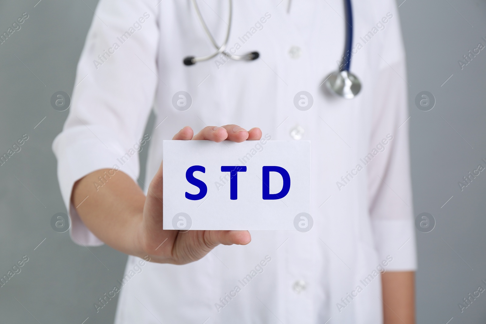 Photo of Doctor holding sheet of paper with abbreviation STD on grey background, closeup