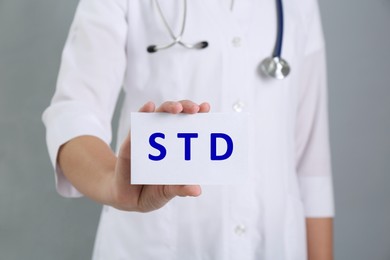 Doctor holding sheet of paper with abbreviation STD on grey background, closeup