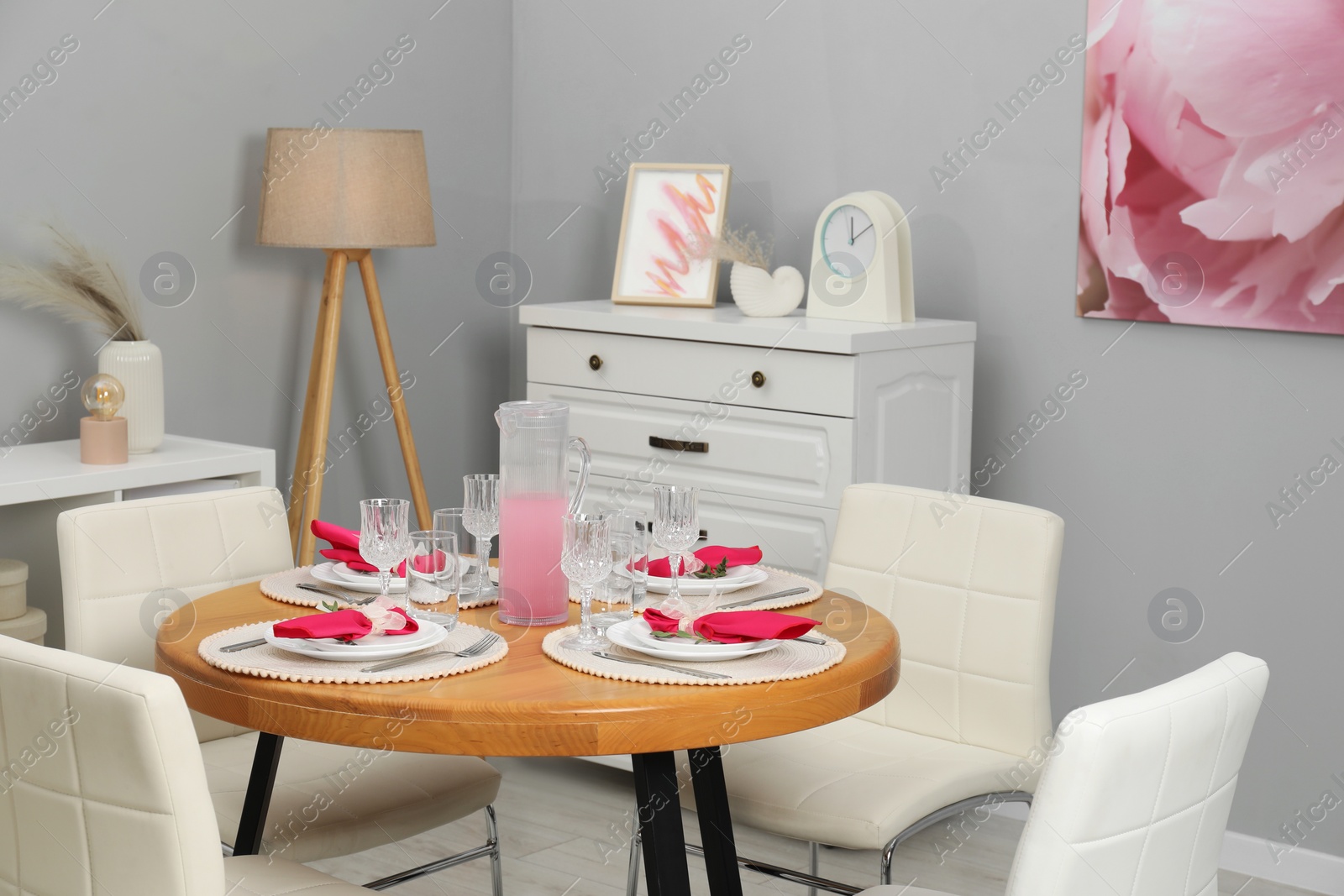 Photo of Color accent table setting. Glasses, plates, jug of beverage and pink napkins in dining room