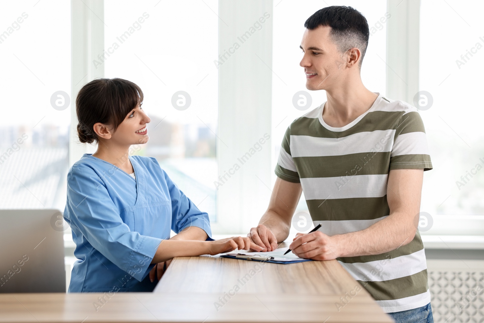 Photo of Smiling medical assistant working with patient at hospital reception