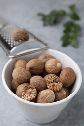 Photo of Nutmegs in bowl on light grey table, closeup
