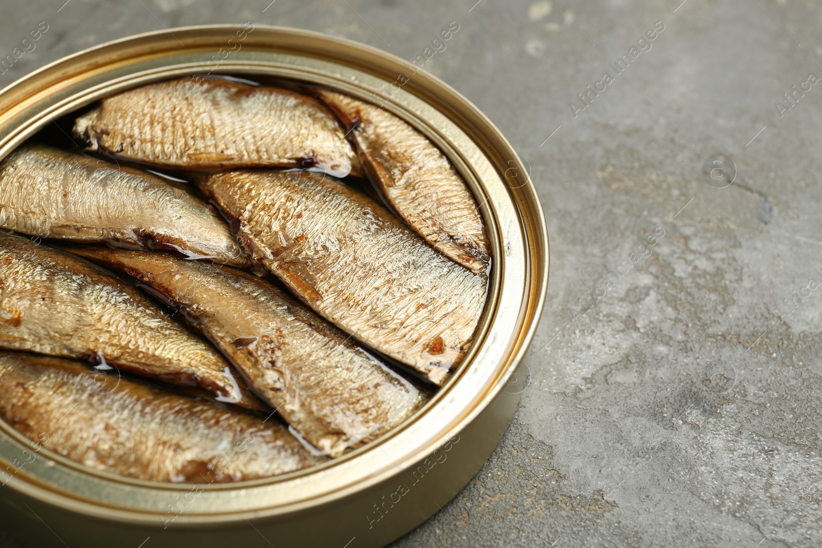 Photo of Sprats in tin can on grey textured table, closeup. Space for text