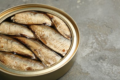 Photo of Sprats in tin can on grey textured table, closeup. Space for text