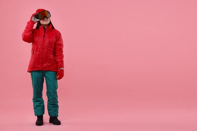 Happy woman in winter sportswear and goggles on pink background. Space for text