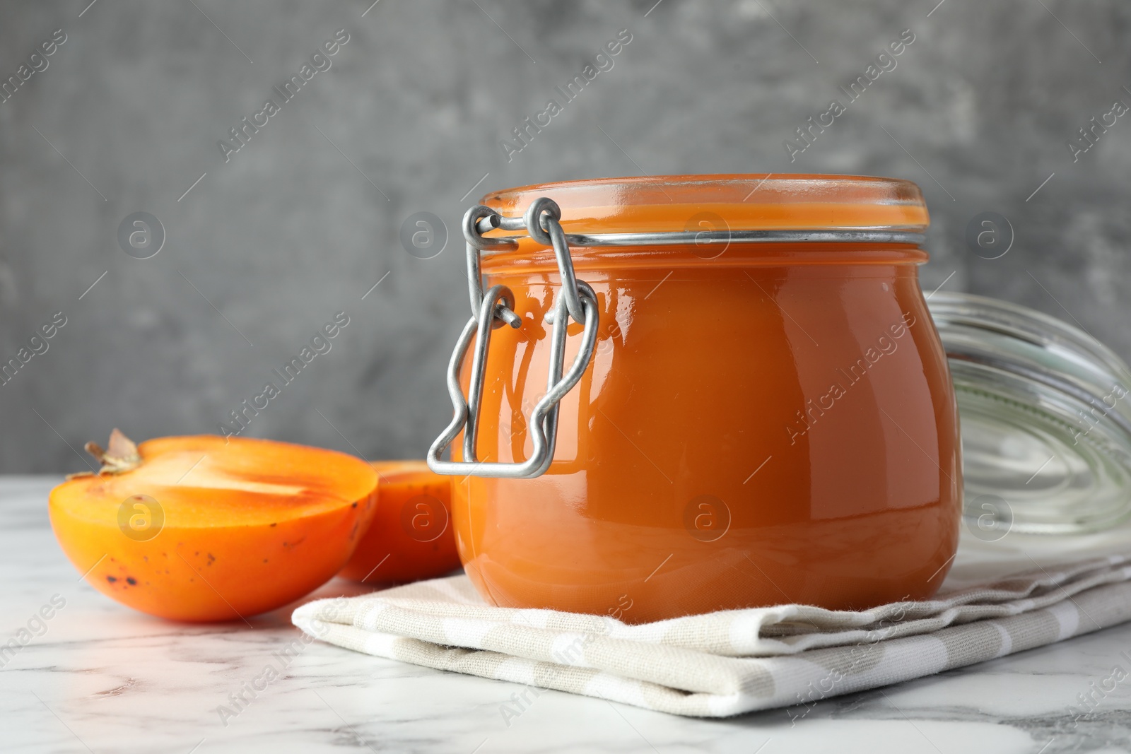 Photo of Delicious persimmon jam and fresh fruits on white marble table, closeup