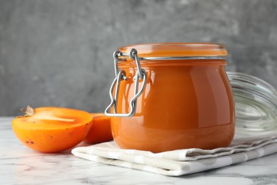 Delicious persimmon jam and fresh fruits on white marble table, closeup