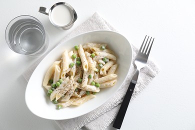 Delicious pasta with green peas, creamy sauce, water and fork on white table, top view