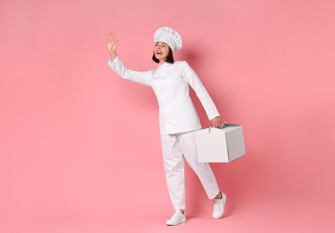 Photo of Happy confectioner with cake box on pink background, space for text