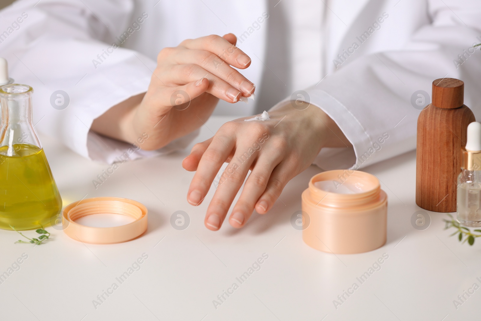 Photo of Dermatologist applying cream onto hand at white table, closeup. Testing cosmetic product