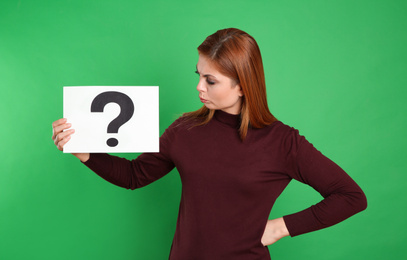 Confused woman holding question mark sign on green background