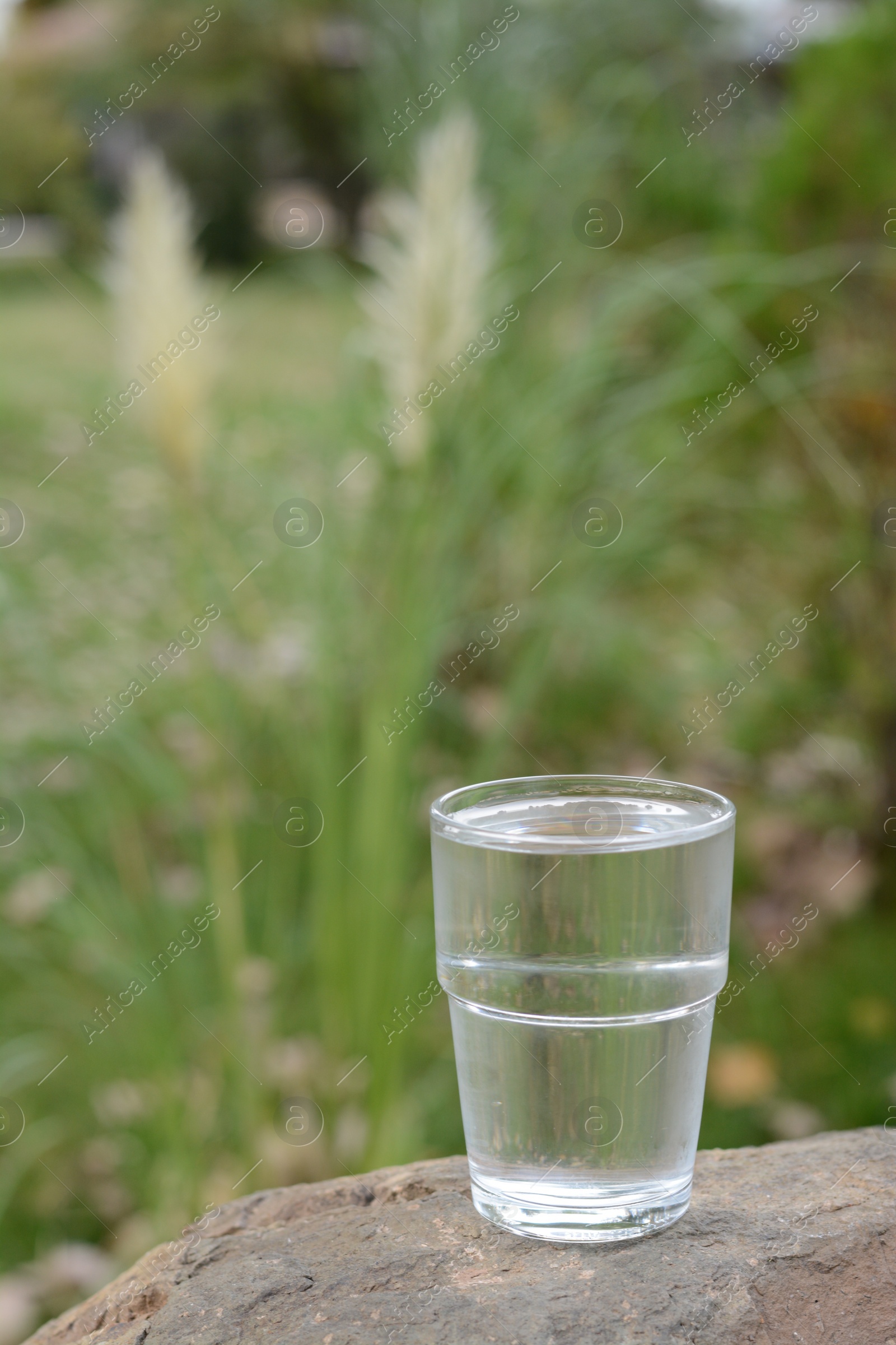 Photo of Full glass of water on stone outdoors, space for text