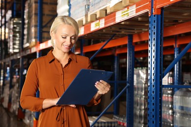 Photo of Happy manager holding clipboard in warehouse with lots of products