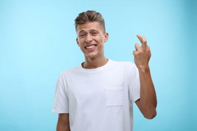 Photo of Emotional young man crossing his fingers on light blue background