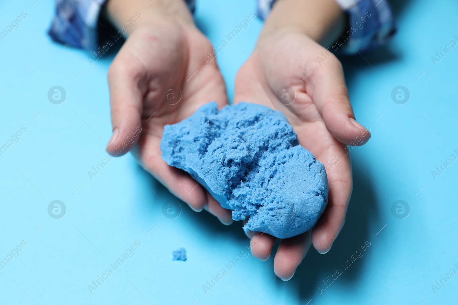 Photo of Woman playing with kinetic sand on light blue background, closeup