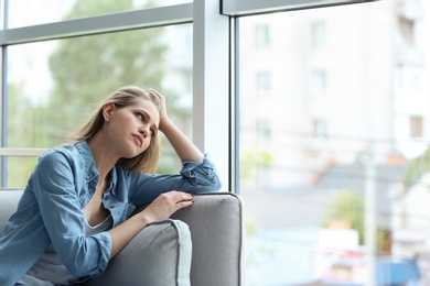 Young sad woman sitting near window at home