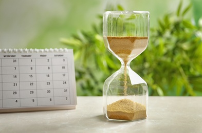 Photo of Hourglass and calendar on table against blurred background. Time management