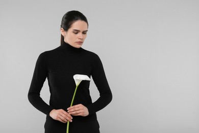 Photo of Sad woman with calla lily flower on light grey background, space for text. Funeral ceremony