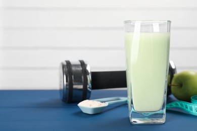 Tasty shake, dumbbell, measuring tape, powder and apple on blue table, closeup with space for text. Weight loss