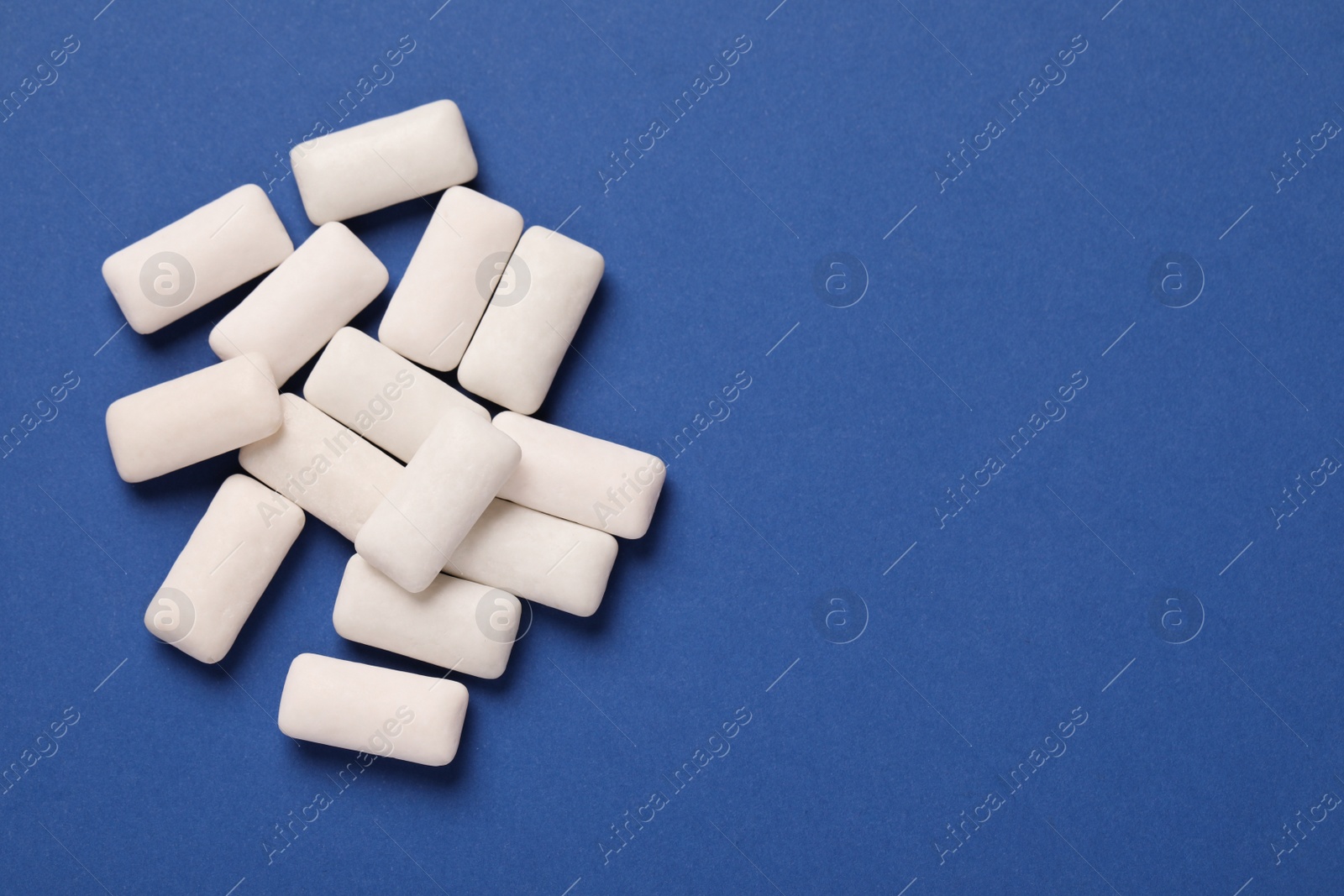 Photo of Many chewing gum pieces on blue background, flat lay. Space for text