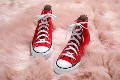 Photo of Pair of stylish red sneakers on faux fur rug