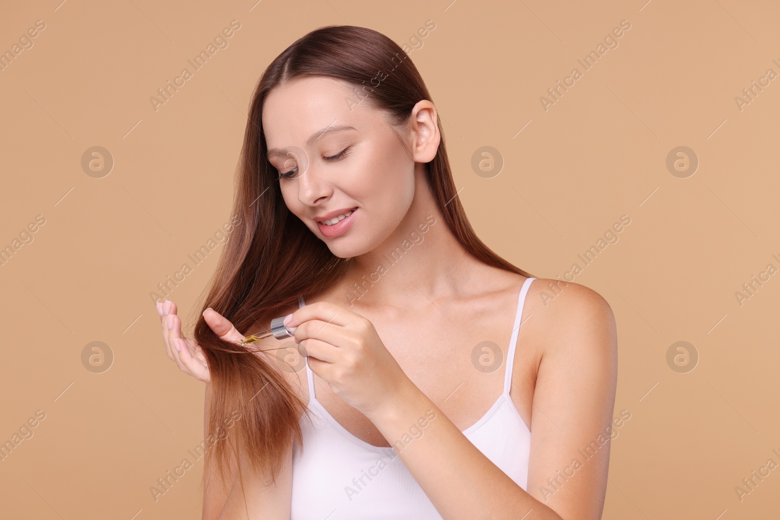 Photo of Beautiful woman applying serum onto hair on beige background