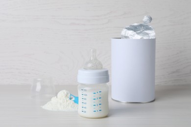 Photo of Blank can of powdered infant formula with scoop and feeding bottle on white wooden table. Baby milk