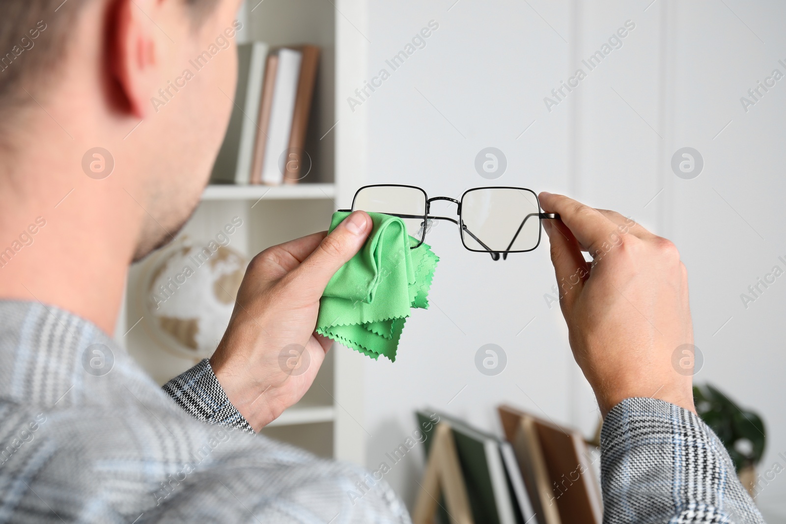 Photo of Man wiping glasses with microfiber cloth indoors